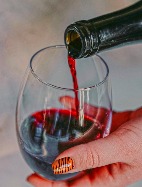 Women with jazzy tiger stripped fingernails cradling a glass of deep red wine whilst being poured 