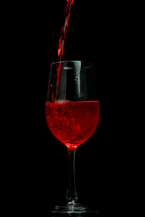 A juicy and vibrant looking red red being poured within a dark and mysterious setting